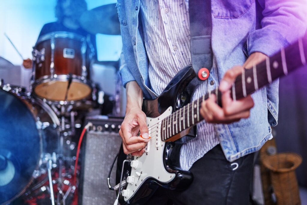 Guitarist playing electric guitar, drummer in background.